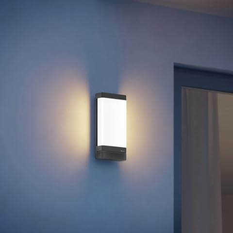 Steinel L 271 Digi C anthracite smart bluetooth outdoor wall light mounted on blue wall, emitting warm glow.