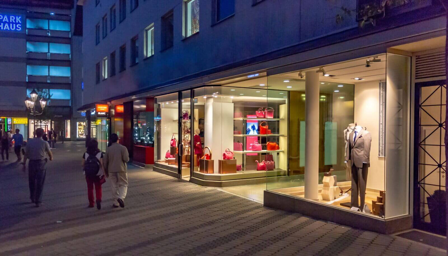 Night view of a stylish store showcasing elegant clothing and accessories, with bright displays and people walking nearby.